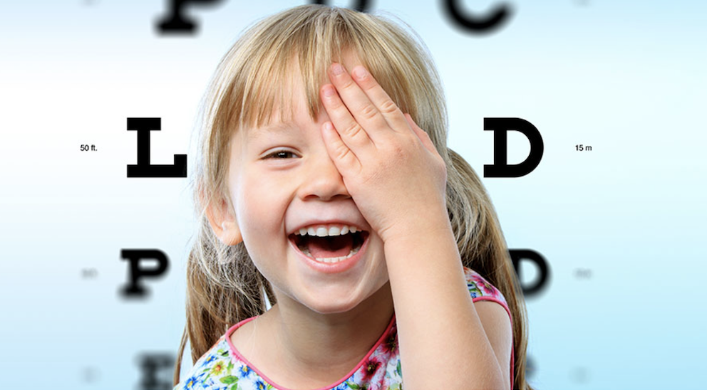 girl covering eye with eye test letters in background